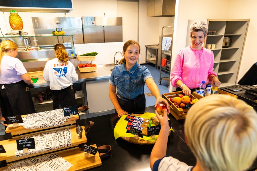 Leerlingen in de kantine met begeleiding, meisje geeft een appel aan een andere leerling