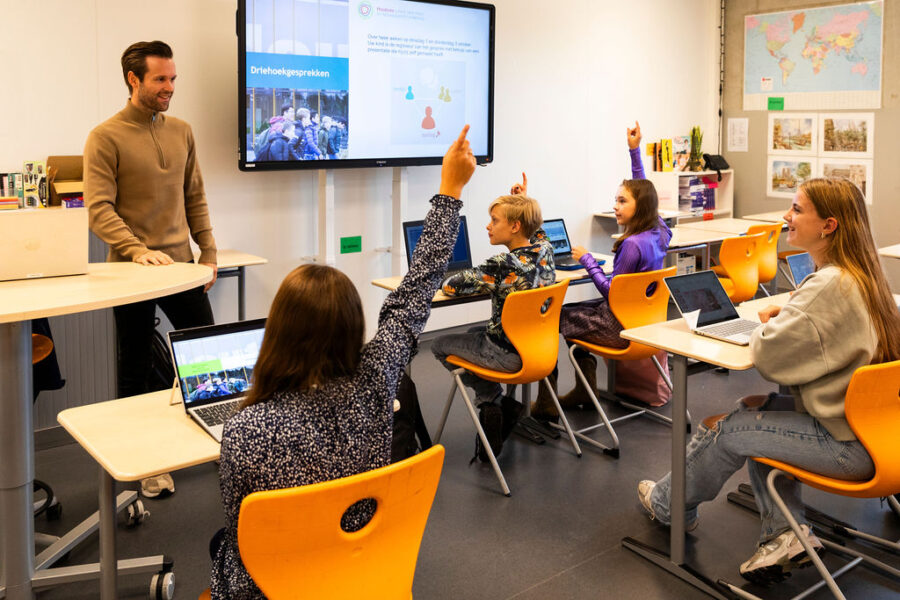 Docent voor de klas in het vmbo, vingers omhoog